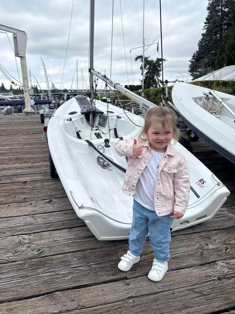 A young member giving a thumbs up beside a dinghy on the dock